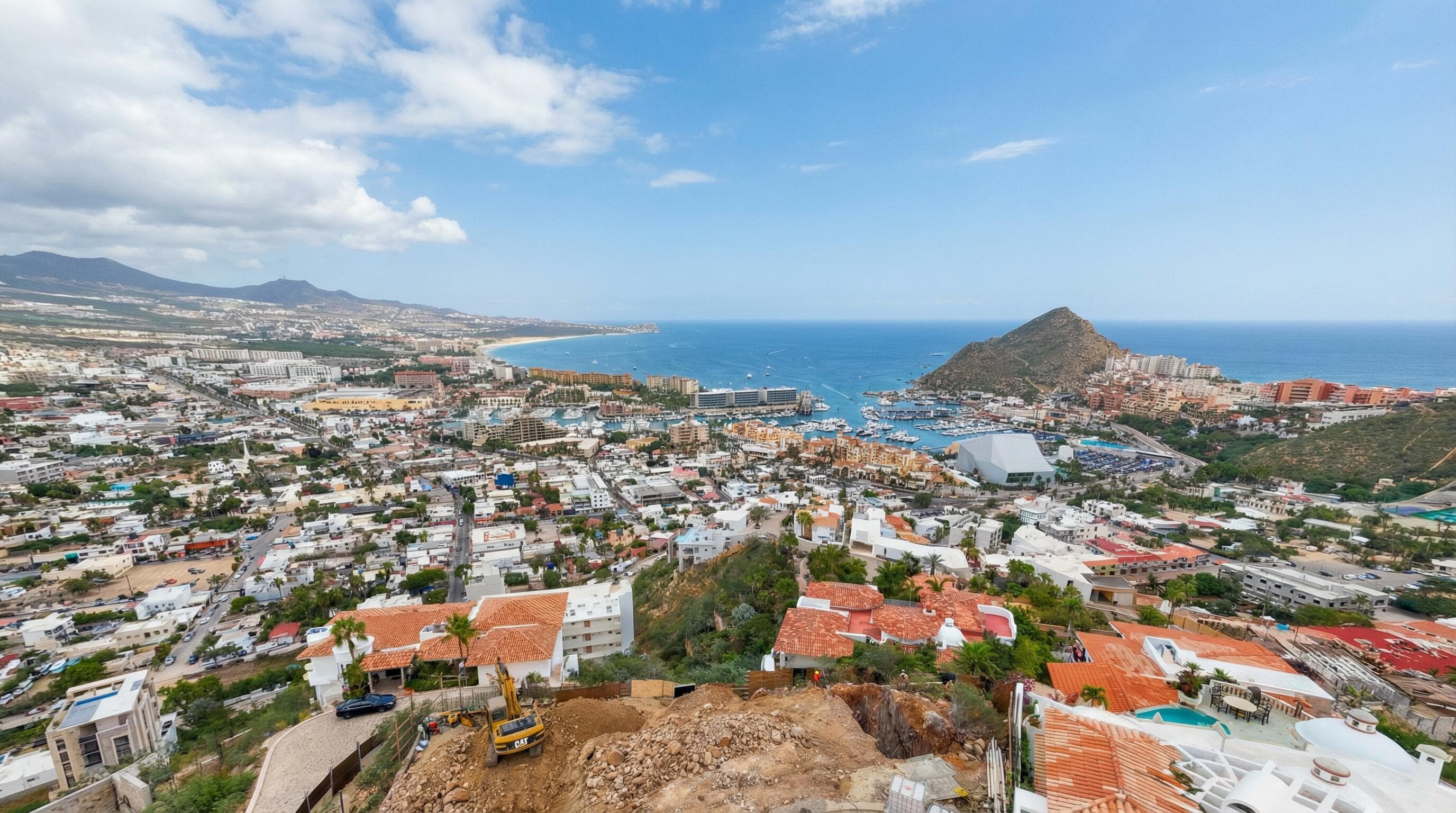Daytime drone from the Villa del León lot in Pedregal, Cabo — excavator, marina, and ocean