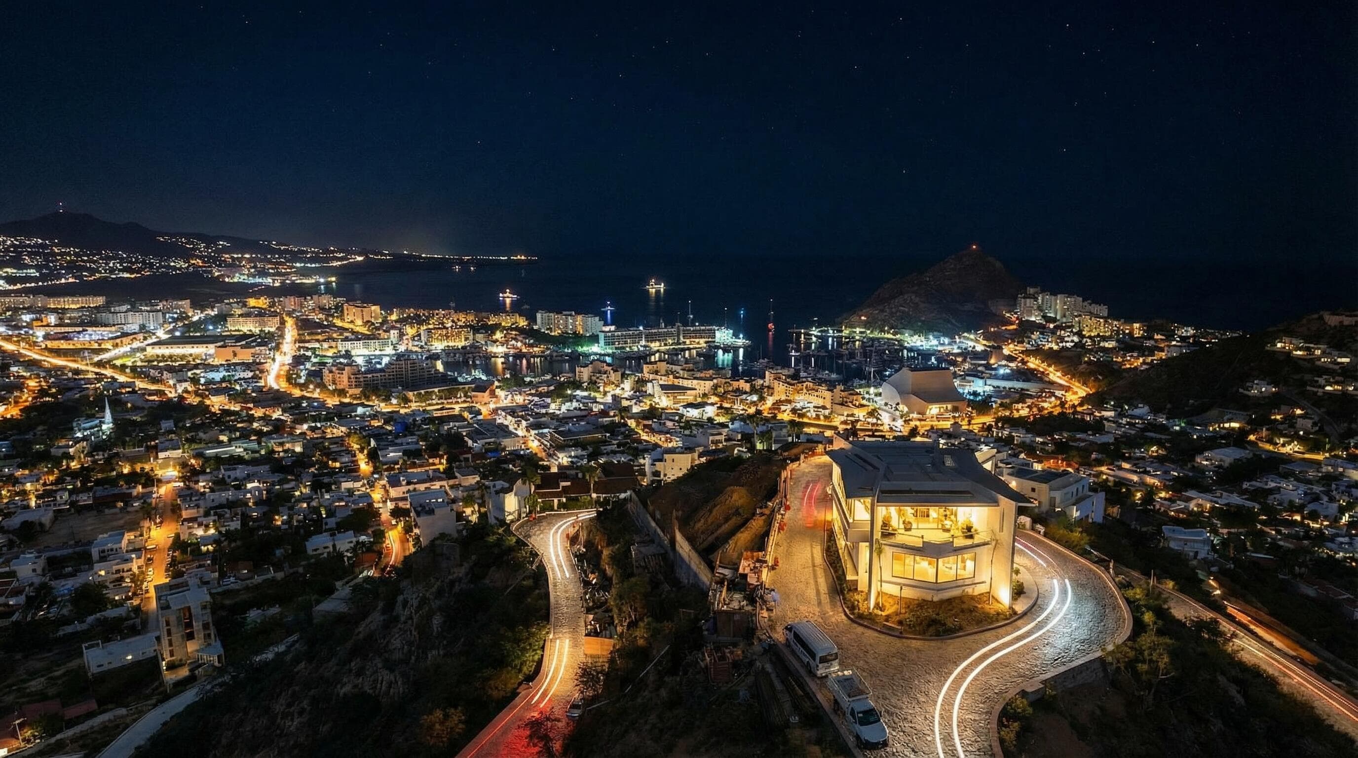 Night drone from the Villa del León lot in Pedregal, Cabo — marina, city lights, and hillside road