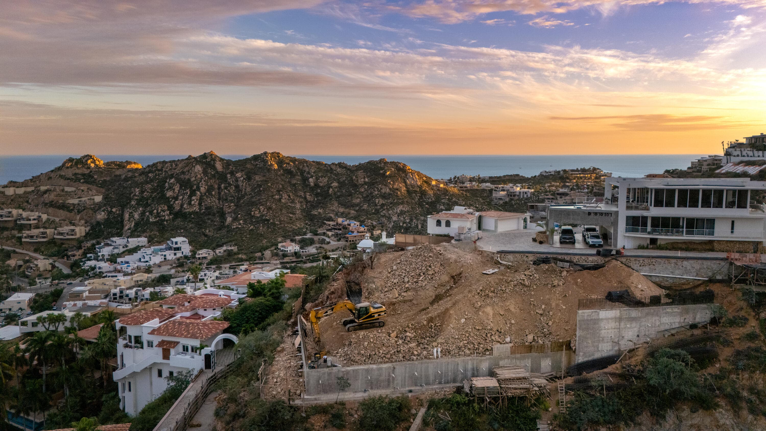 Villa del León foundation walls in Pedregal, Cabo — excavator and ocean on the horizon